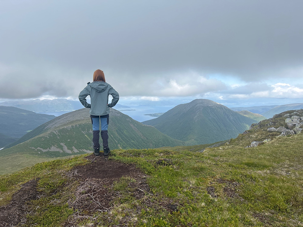 Susanne på det nedtråkkede toppunktet på Frostadtinden og ser mot Oterfjellet, Storhaugen med Tomrefjorden i bakgrunnen.