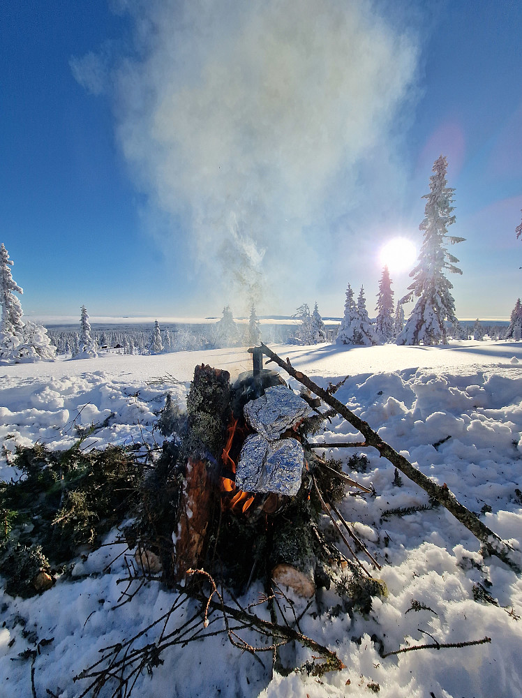 Det var en snøtung skog, men jeg fant litt tørrgran som jeg fikk banket av snøen på og fikk gjort meg opp et bål. Jeg hadde med litt tyri og bjørkenever slik at jeg fikk en liten startvarme. Under slike forhold er det viktig å ta seg god tid med forberedelser av bålet: lage et godt underlag med grove kubber, ta seg tid til å kløve opp kabbene i småved. Da blir det små regel et bra bål.