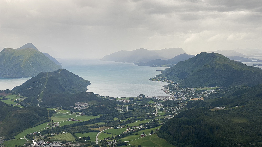 Bilde #11: Utsikt mot Sjøholt. Til venstre for sentrum sees Gausnestoppen [287 m.o.h.], og til høyre for Sjøholt sees Liafjellet [528 m.o.h.]. På sørsida av Storfjorden sees Jogardshornet [693 m.o.h.], Søvikhornet [707 m.o.h.] og Sandvikhornet [876 m.o.h.]. I det fjerne sees på nordsida av fjorden blant annet Merafta [576 m.o.h.] og Sulafjellet [776 m.o.h.].