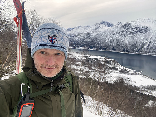 Bilde #2: Med ski og støvler på sekk, på vei oppover mot Breivikskaret og Breiviksetra. Breivika og Isfjorden sees i bakgrunnen.