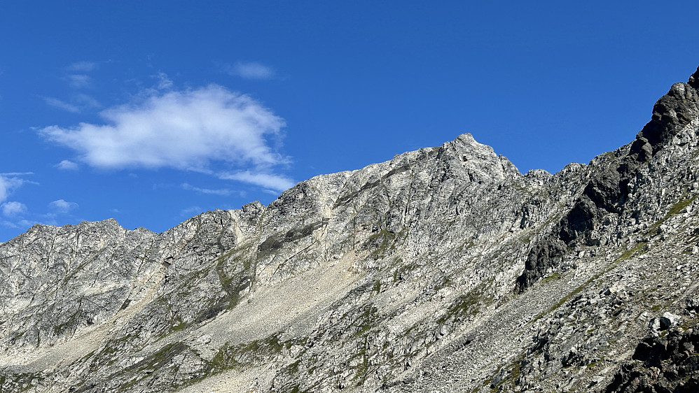 Fjell- og rennepartiene opp mot Solltinden. Midt i bildet den såkalte forkastningsrennen med mye løs grus og stein. Denne rennen går i området der det er er brudd i den skråforløpende , mørke forkastningen. Til venstre (nordvest) for denne, den såkalte vegetasjonslinjen som skal være greiere å gå opp, men hvor en må over noen eksponerte svapartier mot øst for å komme til toppen.