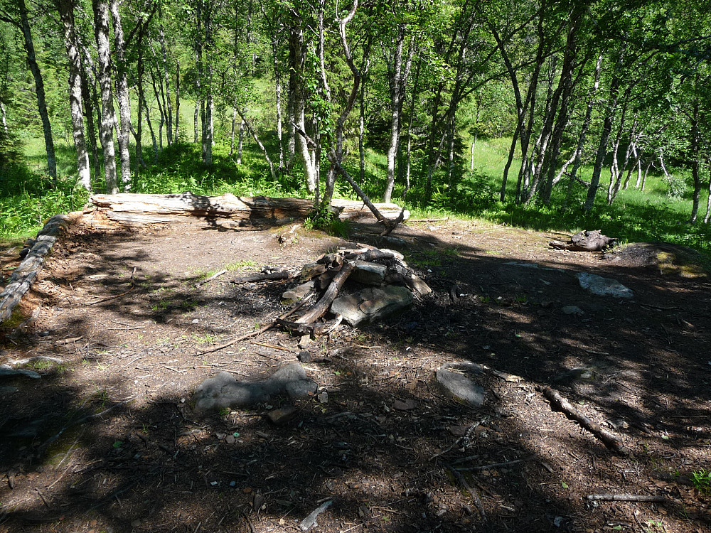 Rester av et gammelt hus med bålplass inni. Lag ved stien opp.