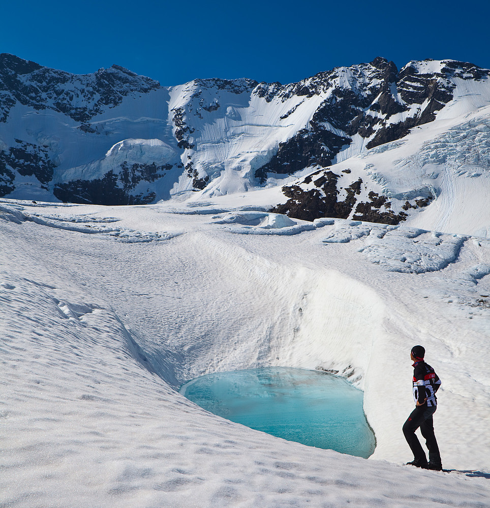 Jørn poserer ved et irrgrønt lite badebasseng på Styggedalsbreen foran Norges kanskje råeste tinde- og brevegg.