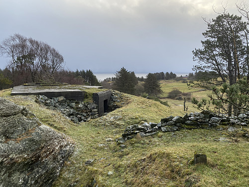 Nærforsvarstilling/bunker heilt sør på fortet. I framgrunnen sjåast to kabelsteinar, og i bakgrunnen skimtast ein koplingsbunker på andre sida av Austre Karmøyveg