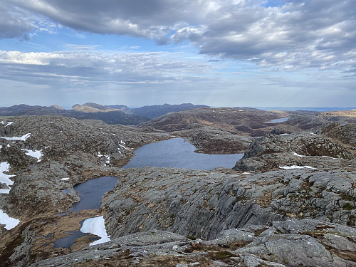 Oppunder 816-toppen sør for Lågahei med utsikt mot bl.a. Litle Gamlestølstjødna og Brogavatnet. Sola skin på kjende toppar i Jørpelandsheia; Heia- og Småsilhodnet og Revafjellet