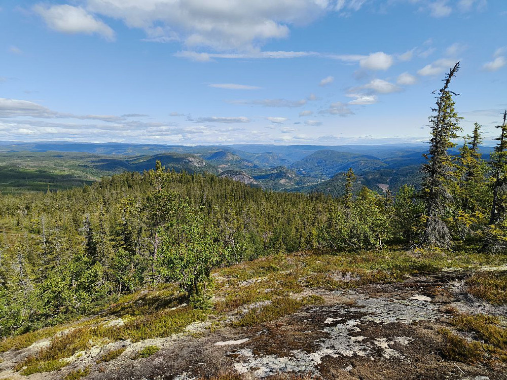 Utsikt fra toppen i retning Begnadalen. Toppen av Kristiansmokollen sentralt i bildet. Jotun-fjell med snø i det fjerne.