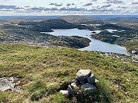 Utsikt fra varden på Blåknuten mot Grunnevasshei, som ligger i sola. Vi ser hytta og varden på toppen.