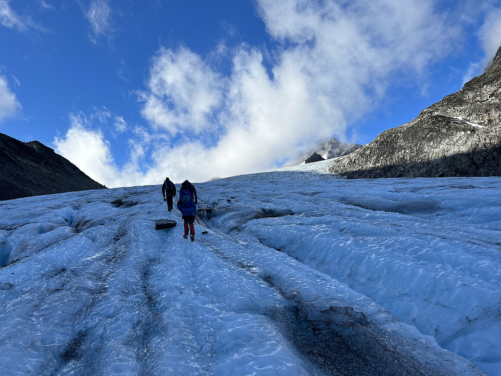 Rolig start nederst på breen med langsgående sprekker. Enkelt oppover her med stegjern. Begynner også å ane noen spisse fjelltopper der oppe.