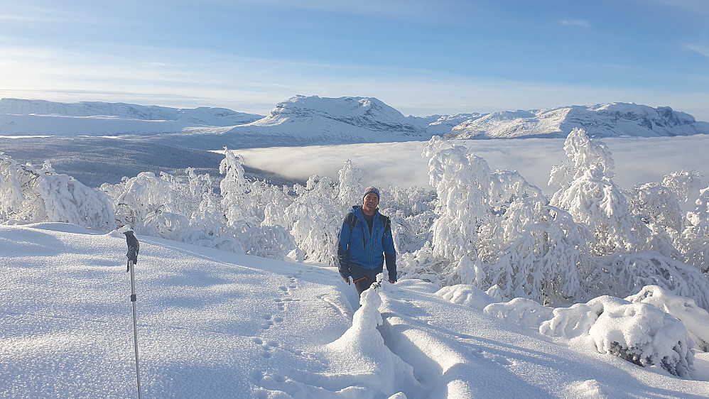 En fornøyd Morten på vei ut av den snøtunge skogen. Herfra var det stort sett snaufjell videre til topps. Grindane (1724) dominerer bakgrunnen midt i bildet.