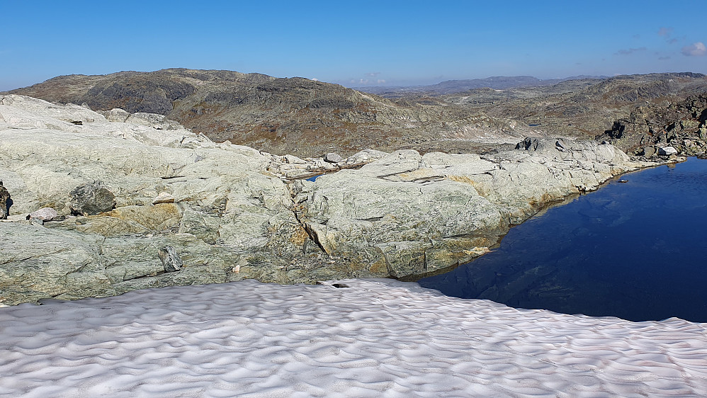 Et bitte lite tjern som fremdeles var delvis dekket av en snøfonn, på ryggen mellom Urevassnutane (1770) og Tyrvlesvatnet. Fjellet bak til venstre er Langvasseggi (1669).