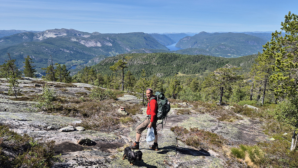 Vi har kommet opp til området hvor stien følger en bred rygg med en del svaberg. Her med utsikt mot vest. Nærmeste ås rett over Øyvind, er Godokkfjellet (612), som vi besøkte litt tidligere. Vannet lengre bak som ligner en fjord, er Bandak. Fjellet til venstre med store svabergvegger, er Roholtfjellet.